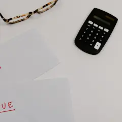 Okulary, kalkulator i kartki z napisami "PAID" i "DUE" na białym tle.