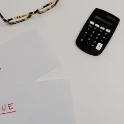 Okulary, kalkulator i kartki z napisami "PAID" i "DUE" na białym tle.