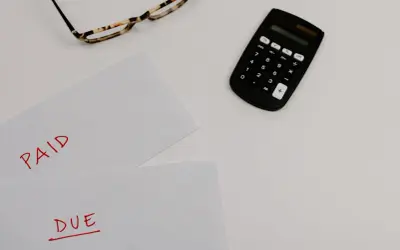 Okulary, kalkulator i kartki z napisami "PAID" i "DUE" na białym tle.