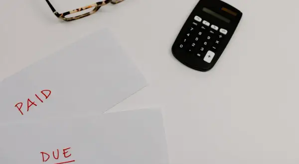 Okulary, kalkulator i kartki z napisami "PAID" i "DUE" na białym tle.